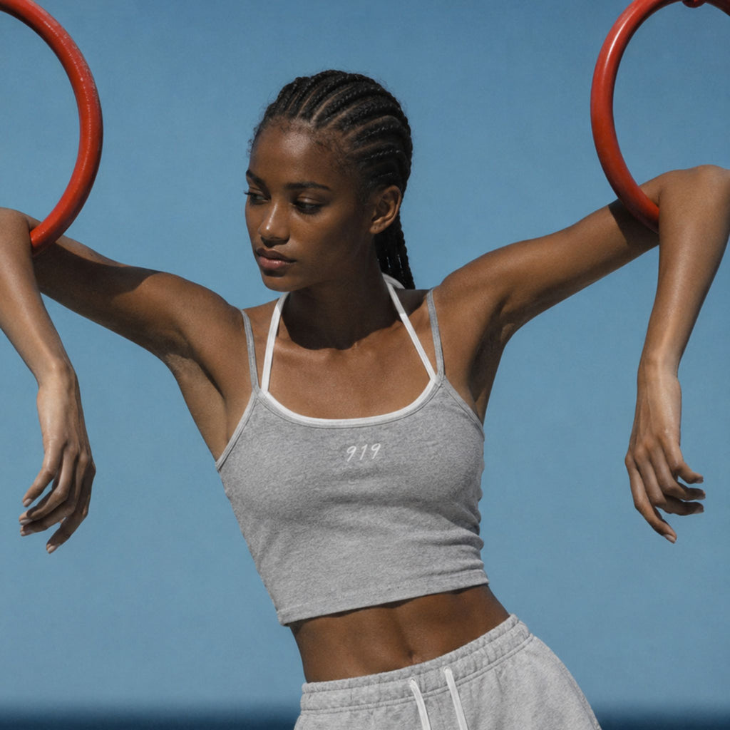 Woman exercising with red rings against a clear blue sky wearing a grey crop top